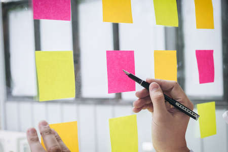 Young creative professional leader using post it notes in glass wall to writing strategy business plan, management and people concept.の写真素材