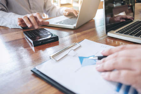 Two business persons working at office desk and discussing using laptop to ideas of project about company offer, they is pointing on a contract and giving explanations, team of successful people.の写真素材