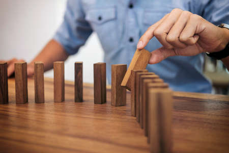 Risk and strategy in business, Close up of businessman hand gambling placing wooden block on a line of domino.の写真素材