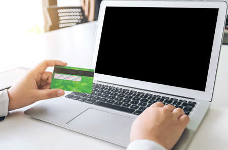 Business woman holding credit card entering security code and using laptop computer and digital...