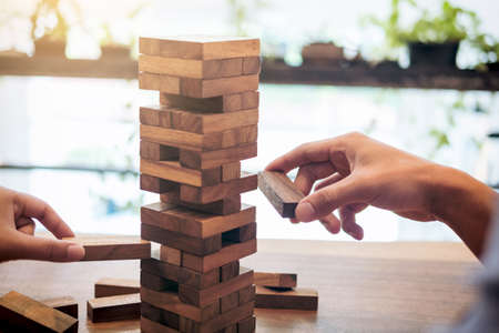 Images of hand of businesspeople placing and pulling wood block on the tower, Alternative risk...