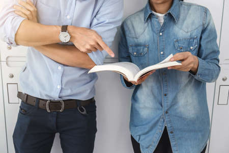 Cheerful young student standing holding book and reading, classmates helps friend catching up...