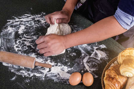 Raw dough for bread with ingredients on black background, male hands kneading dough sprinkled with flour table.の写真素材
