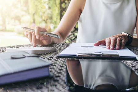 Work and relax, Woman freelancer is working new project of business stragegy plan and using calculator to analysis information data, while sitting garden scenery outdoor background.の写真素材