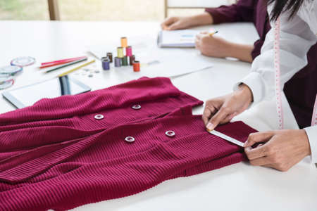 Two young dressmaker or designer colleagues working as fashion designers and drawing sketches for clothes, choose color bar in tablet, profession and job occupation, Fashion Designer Stylish Concept.の写真素材