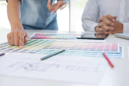 Two interior design or graphic designer at work on project of architecture drawing with work tools and color swatches, colour chart, color samples for selection, renovation and technology concept.の写真素材
