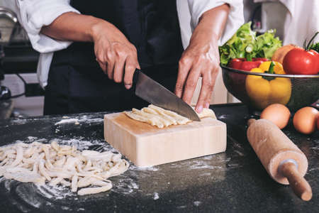 female housewife making homemade pasta with flour and eggs over table in kitchen.