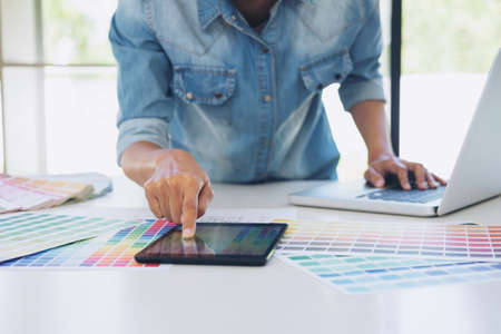 Color samples, colour chart, swatch sample, Graphic designer being selecting Color table and graphics tablet, pen at workplace with work example on wooden desk.の写真素材