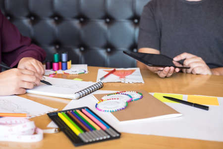 Two young professional Fashion designer colleagues working and project of drawing sketches for clothes in workplace with laptop, digital tablet and color charts, Fashion Designer Stylish Concept.の写真素材