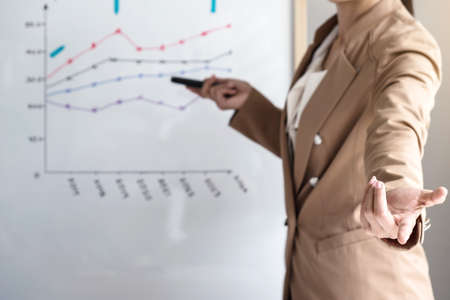 Business woman leader making presentation with her colleagues, pointing to the graph on board and...