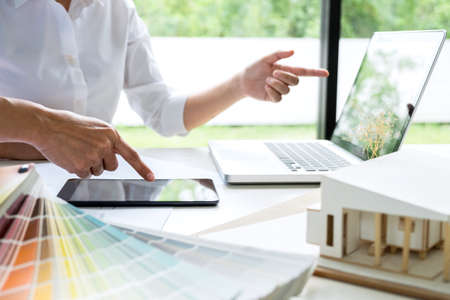 Two young women interior design or graphic designer working on project of architecture drawing with work tools and color swatches, colour chart in digital tablet at workplace.の写真素材