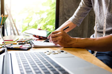 Fashion Designer Stylish Concept, Young dressmaker or designer drawing design sketch working for clothes and Choose color bar in digital tablet in manufacturing office studio.の写真素材