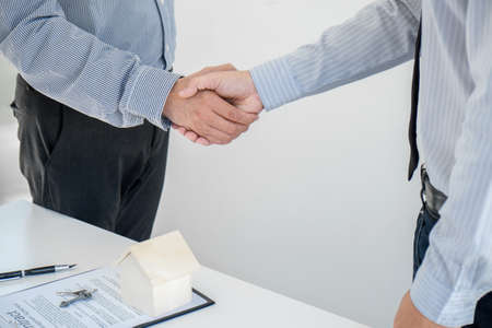 Home loan insurance concept, broker agent shaking hands with customer after good deal agreement, home model.の写真素材