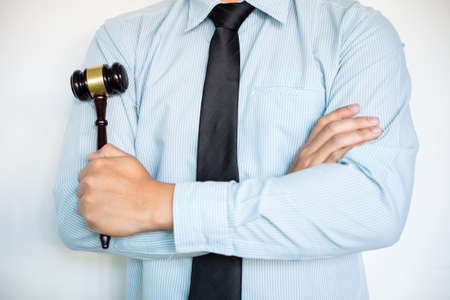 Close-up of Male lawyer with arm crossed standing front background and action hammer or gavel in hand.の写真素材
