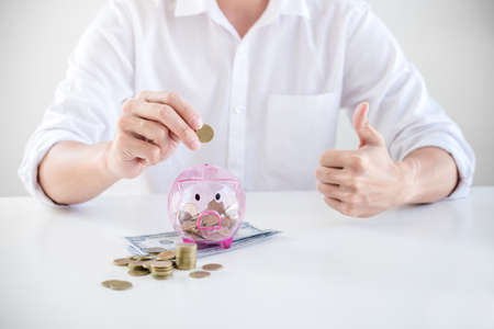 Businessman putting coins into piggy bank and using calculator to analysis business investment...