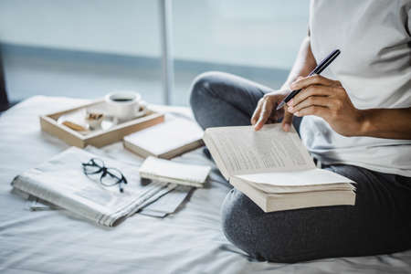 Young woman happiness on bedroom in enjoying reading books, newspaper and writing diary in holiday...