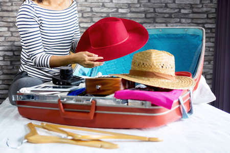 Travel and vacation concept, happiness young woman packing a lot of her clothes and stuff into suitcase on bed prepare for travel and journey trip in holiday.の写真素材
