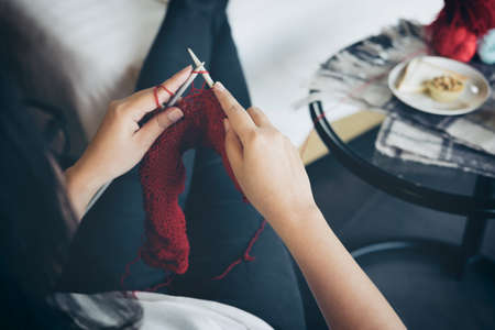 Close up shot of young woman hands knitting a red scarf handicraft in the living room on terrace at home.の写真素材