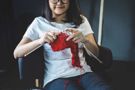 Close up shot of young woman hands knitting a red scarf handicraft in the living room on terrace at home.の写真素材