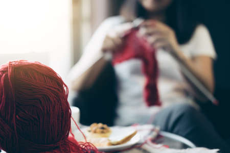 Close up shot of young woman hands knitting a red scarf handicraft in the living room on terrace at home.の写真素材