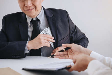 Bribery and corruption concept, bribe in the form of dollar bills, Businessman giving money while making deal to agreement a real estate contract and financial corporate.の写真素材