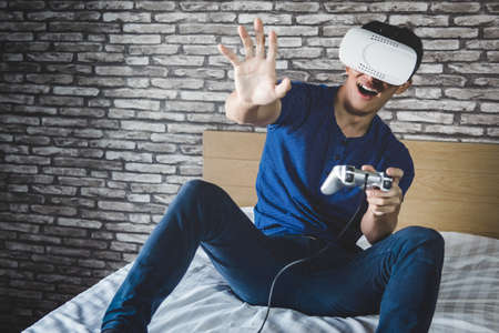 Young man in virtual reality headset or 3d glasses playing video game and pointing in the air,...