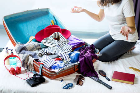 Travel and vacation concept, happiness woman packing stuff and a lot of clothes into suitcase on bed...