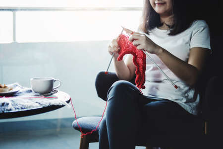 Close up shot of young woman hands knitting a red scarf handicraft in the living room on terrace at home.の写真素材
