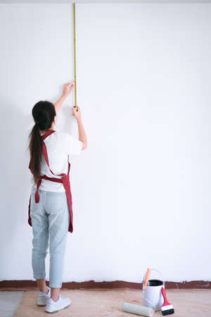 Interior working, female painter with measure tape checking wall length in room, shape and structure.の写真素材