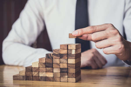 Risk To Make Business Growth Concept With Wooden Blocks, hand of man has piling up and stacking a wooden block, Alternative risk concept, plan and strategy in business.の写真素材