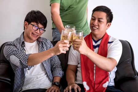 Young Happy Asian Men family or football fans watching soccer match on tv and cheering football team, celebrating with drink beer and eat popcorn at home, sports and entertainment concept.の写真素材