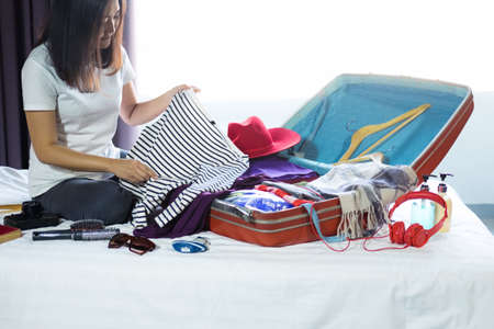 Travel and vacation concept, happiness woman packing stuff and a lot of clothes into suitcase on bed...