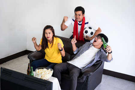 Group of friends fanclub watching soccer match on tv and cheering football team, celebrating with...