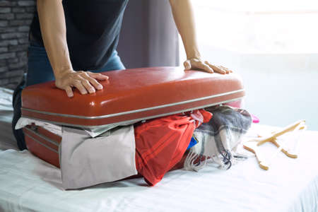 Travel and vacation concept, happiness young man packing a lot of his clothes and stuff into suitcase on bed prepare for travel and journey trip in holiday.の写真素材