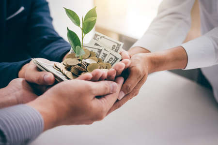 Hands of business team holding plant sprouting growing from golden coins and banknotes, business investment and strategy concept.の写真素材