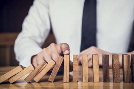 Strategy and successful intervention concept for business, businessman hand Stopping Falling wooden Dominoes effect from continuous toppled or risk.の写真素材