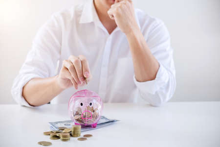 Businessman putting coins into piggy bank and using calculator to analysis business investment strategy with income of money coin and dollar, financial concept.の写真素材