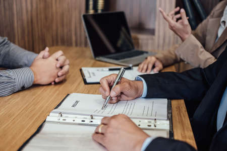 Two senior manager reading a resume during a job interview, Employer interviewing to ask young male job seeker for recruitment talking in office.の写真素材