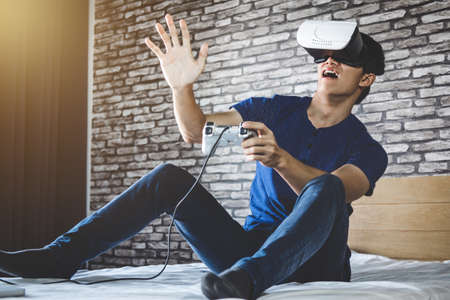Young man in virtual reality headset or 3d glasses playing video game and pointing in the air,...