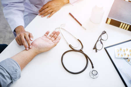 Doctor in white coat taking and checking the Patient's wrist pain during the examination.