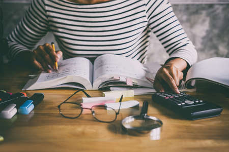 Young student sitting at desk in home studying and reading, doing homework and lesson practice...