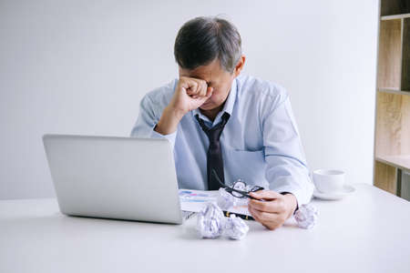 Feeling sick and tired, Senior businessman depressed and exhausted, businessman at his desk frustrated with problems and keeping eyes closed while sitting on office.の写真素材