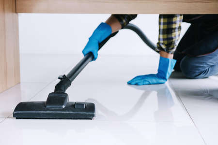 Housekeeping and housework cleaning concept, Happy young man in blue rubber gloves using a vacuum cleaner on floor at home.の写真素材