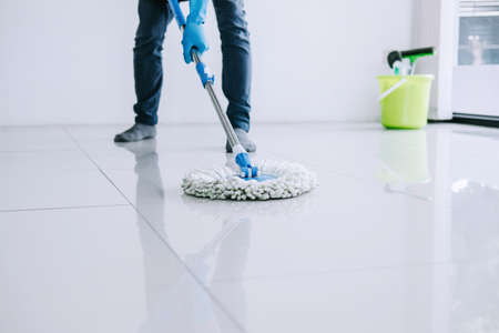 Husband housekeeping and cleaning concept, Happy young man in blue rubber gloves wiping dust using mop while cleaning on floor at home.の写真素材