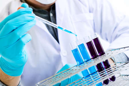 Biochemistry laboratory research, Scientist or medical in lab coat holding test tube with reagent with drop of color liquid over glass equipment working at the laboratory.の写真素材