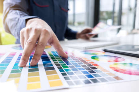 Male creative graphic designer working on color selection and color swatches, drawing on graphics tablet at workplace with work tools and accessories.の写真素材