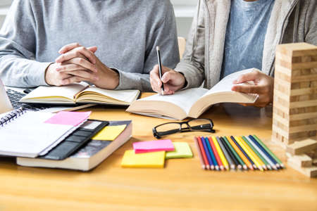 High school tutor or college student group sitting at desk in library studying and reading, doing...