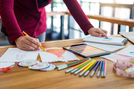 Young woman designer working as fashion designers at work with fashion sketches and color charts,...