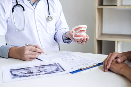 Male doctor or dentist writing report working with tooth x-ray film model and equipment used in the treatment of dental and dentistry and recommend patient at workplace.の写真素材