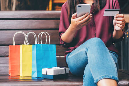 Consumerism, shopping, lifestyle concept, Young woman sitting near shopping bags and gift box while payment by smartphone enjoying in shopping.の写真素材